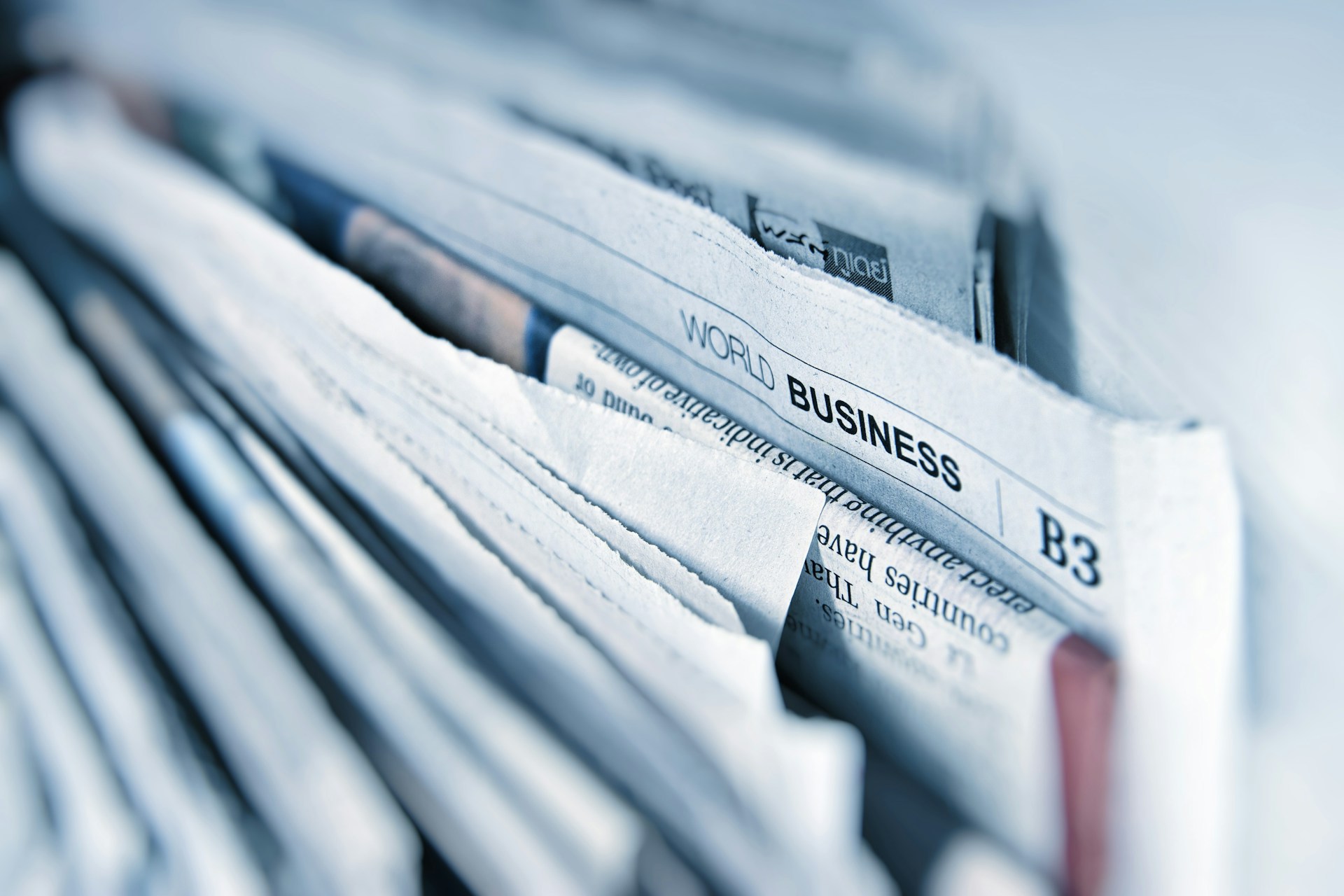 A newspaper spread open on a desk beside reading glasses